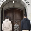 Candidats devant la porte d'entrée de la Légion Étrangère, surveillés par un militaire en uniforme.